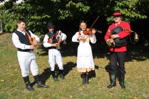 zdjęcie: czworo młodych muzyków z instrumentami ludowymi na tle zieleni parku