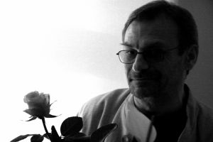 Zdjęcie czarno-białe przedstawiające portret mężczyzny w okularach, trzymającego w ręku różę